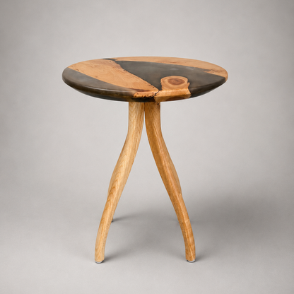 A small round wooden side table with three curved legs, featuring a dark and light wood grain pattern on the tabletop, photographed against a neutral gray background.