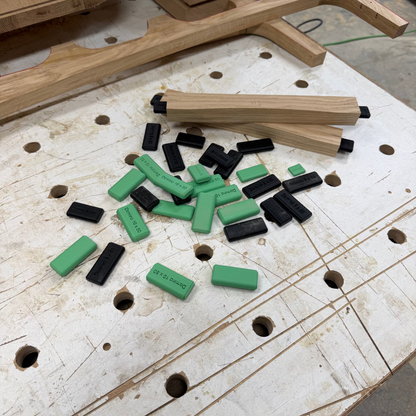 A workshop table with a pile of dry-fit festool dominos, with a light wood bow-like object and other wooden pieces in the background.