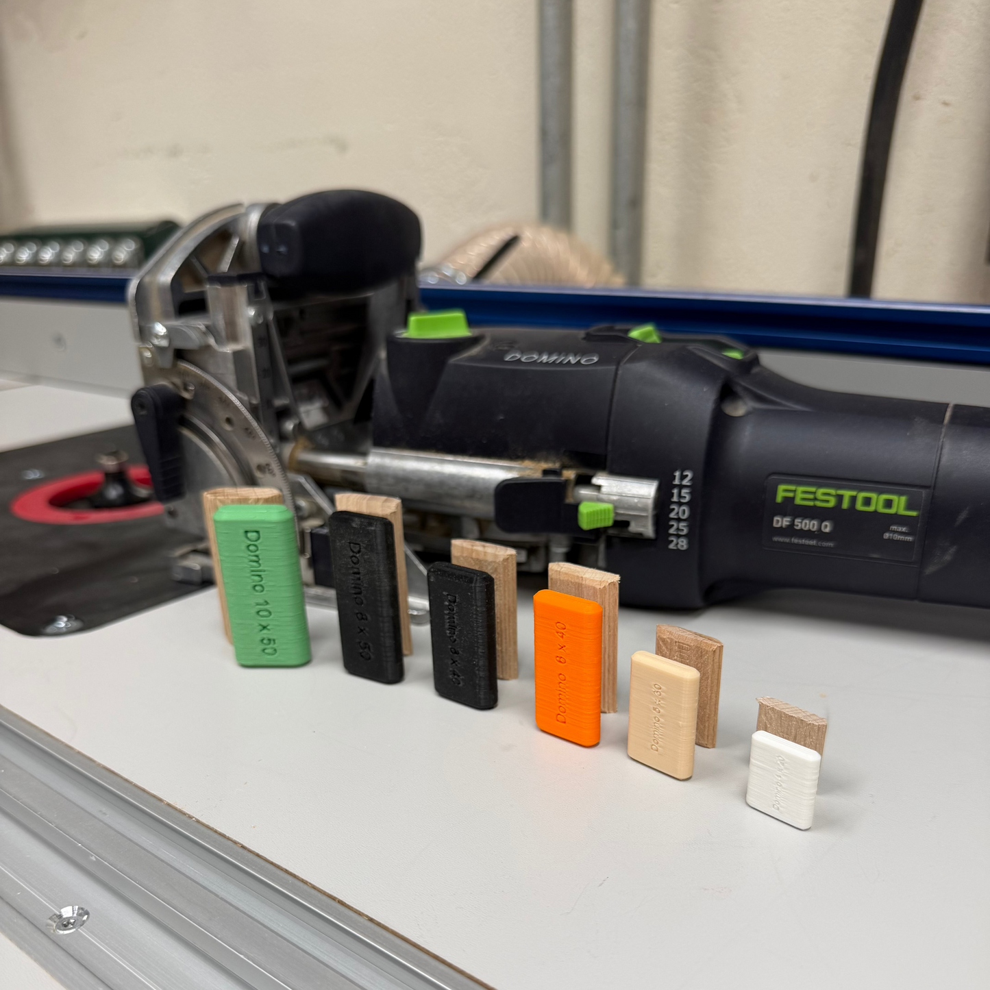 A Festool Domino DF 500 with several dry fit dominos in different colors arranged in front of the tool.