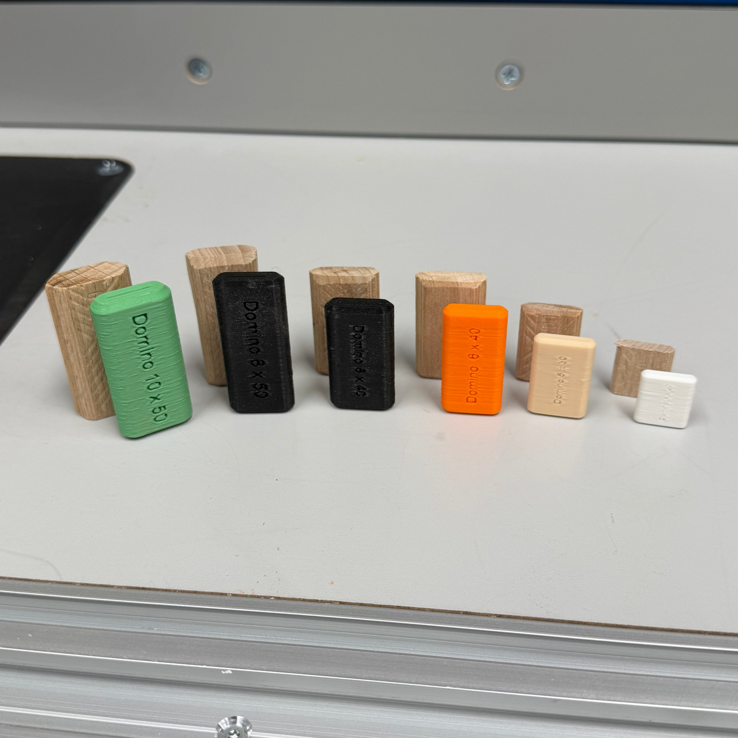 A row of small rectangular 3D-printed objects in various colors including green, black, orange, beige, and white, arranged on a light gray tabletop.