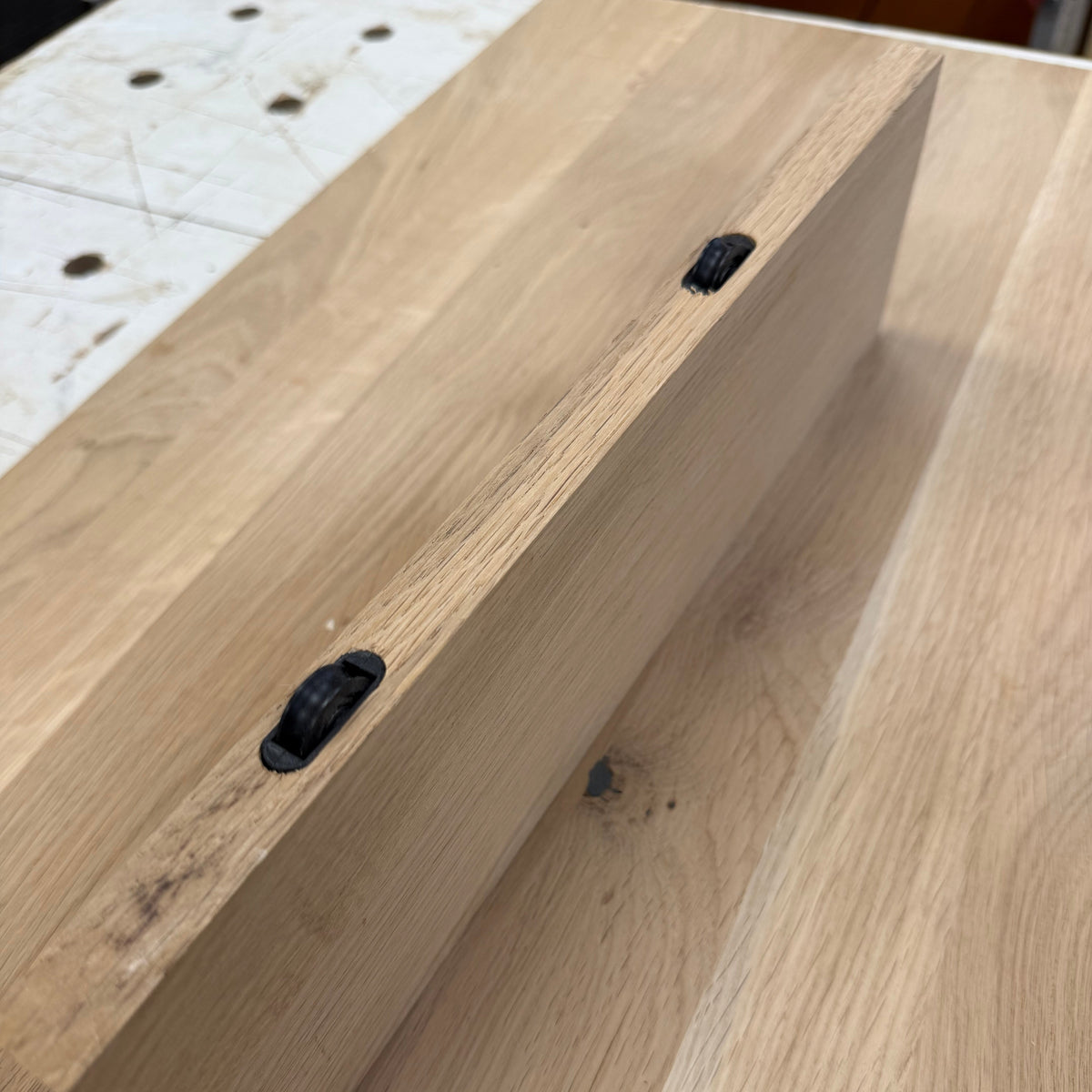 A close-up of a light natural wood drawer or cabinet front with two black metal drawer pulls installed, resting on a matching wood tabletop.