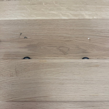 Close-up of a light oak wood surface with visible wood grain, plank seams, and two small dark circular hardware pieces near the lower middle.